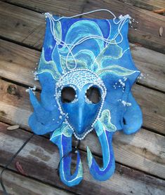 a blue mask with pearls on it sitting on top of a wooden floor next to a string