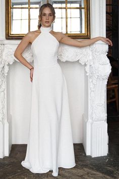 a woman standing in front of a window wearing a white dress and posing for the camera