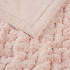 a pink blanket laying on top of a bed next to a white pillow and blanket