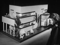 a woman looking at a model of a house with furniture on the outside and inside