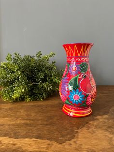 a colorful vase sitting on top of a wooden table next to a potted plant