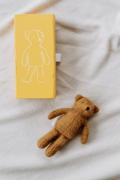 a brown teddy bear laying on top of a bed next to a small yellow book