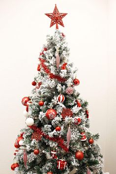 a white christmas tree with red and silver ornaments on it's branches, in front of a white wall