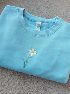 a blue t - shirt with a flower embroidered on the front and side, laying on carpet