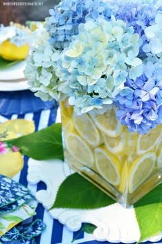 blue and yellow flowers in a square vase on a table with plates, napkins and place mats