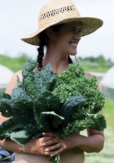 a woman wearing a straw hat holding a bunch of green leafy vegetables in her hands