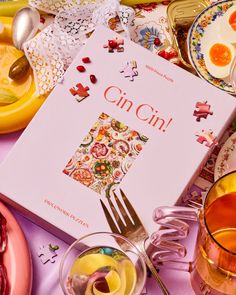 a table topped with plates and cups filled with food next to a book on the cover