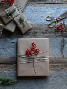 wrapped presents with red berries and twine tied to them on a wooden table next to scissors