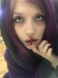 a woman with purple hair and piercings on her nose is posing for the camera