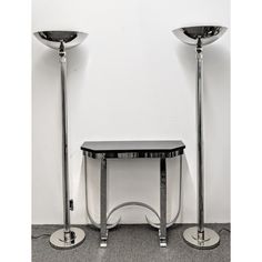 two metal lamps sitting next to each other on top of a floor in front of a white wall