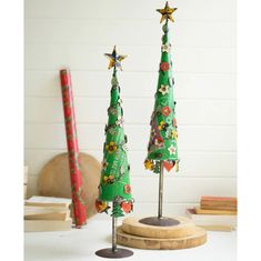 two green christmas trees with flowers and stars on them sitting on a table next to books