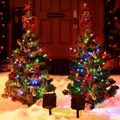 two small christmas trees in front of a door with lights on them and presents under the tree