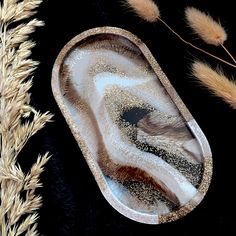 an agate glass dish with gold flecks sits on a black surface next to dry grass