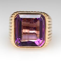 This amazing ring features a fluted design and is accented with one (1) emerald cut natural amethyst set into a bezel setting. The ring measures 16.1mm at the top, rises 7.6mm above the finger, tapering to 6.3mm wide and 1.3mm thick at the base of the shank. It is currently a size 4.75. Luxury Yellow Gold Amethyst Ring With Emerald Cut, Luxury Emerald-cut Amethyst Ring For Formal Events, Luxury Emerald Cut Amethyst Ring For Formal Occasions, Luxury Gemstones With Bezel Setting For Formal Occasions, Luxury Bezel Set Gemstones For Formal Occasions, Luxury Formal Gemstones With Bezel Setting, Luxury Purple Ring With Bezel Setting, Baguette Cut Amethyst Ring For Formal Occasions, Luxury Amethyst Ring Emerald Cut