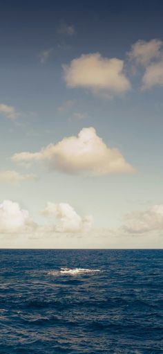 an airplane flying over the ocean on a cloudy day with blue sky and white clouds