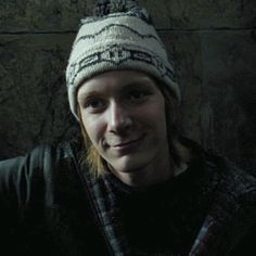 a woman wearing a hat and scarf posing for a photo in front of a stone wall