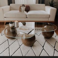 a dog sitting on top of a white couch next to a glass table with two vases