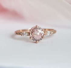 an engagement ring with a pink diamond and two white diamonds on the band, set in gold