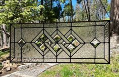 a stained glass window hanging from the side of a tree in front of some trees