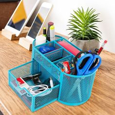 two blue baskets with pens, scissors and other items in them on a table next to a potted plant