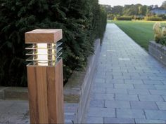 a light that is sitting on the side of a sidewalk next to some bushes and trees