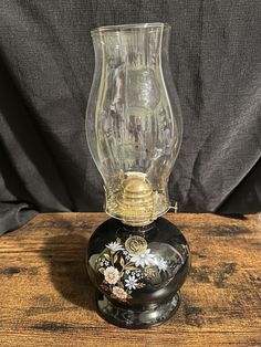 a glass vase sitting on top of a wooden table next to a black container with flowers painted on it