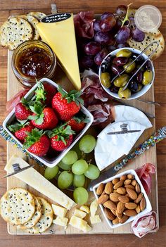 a wooden table topped with cheese, fruit and crackers