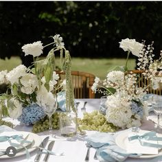 the table is set with white and blue flowers in vases, silverware, and napkins