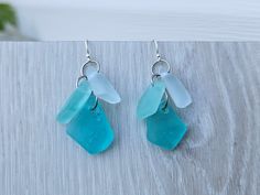 two pieces of sea glass are hanging from silver earwires on a wooden surface