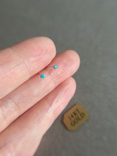 a person's left hand holding a tiny blue nose pin with the word mom on it