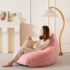 a woman sitting on a pink bean bag chair in a white room with a lamp