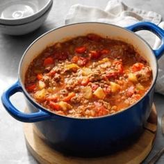 a blue pot filled with stew on top of a wooden cutting board next to silverware