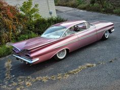 an old pink car is parked on the street