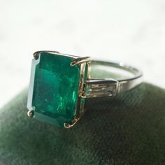 This stunning ring features a GIA certified 4.23 carat step cut emerald and diamond accents in 14 karat yellow gold and platinum. The impressive center stone features a rich sea green hue and is set in a four pronged 14 karat yellow gold basket. With elongated facets and tapered corners, the emerald is accented by two (2) .25 carat baguette cut diamonds. The diamonds are near colorless and visually complement the shimmering platinum band. This fabulous right hand ring features a subtle two-toned Diana Engagement Ring, Gold Basket, Emerald Ring Vintage, Right Hand Ring, Emerald And Diamond Ring, Antique Diamond Rings, Emerald Diamond Ring, Hand Ring, Step Cut