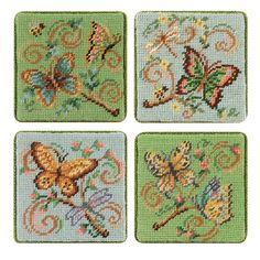 four cross stitch coasters with butterflies and flowers on green fabric, each decorated in different colors