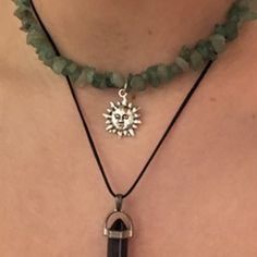 a woman wearing a green necklace with a silver sun charm