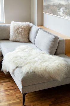 a couch with white fur on it in front of a window and wood flooring