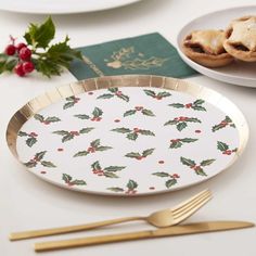 a plate with holly and berries on it next to gold utensils, silverware and a passport