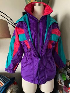 "DESCRIPTION * Vintage 80s Team Sun Ice Long Ski Jacket * Deep Side Pocket with Fun Zipper Closures * High Collar with Zipper and Button Closure *Purple Base with Fun Neon Colorblocking! *Attached hood that can be hidden in zipper closure at neckline! *Perfect to throw over any outfit for Colorful Look *Can definitely been worn many ways, Perfect for the 80Trends that are happening now!! DETAILS *Label: Sun Ice *Size: Medium to Large, See Measurements Below *Color: Saturated Pink, Turquoise, and Affordable Retro Winter Windbreaker, Winter Patchwork Nylon Windbreaker, Retro Hooded Outerwear For Ski Season, Retro Purple Windbreaker For Fall, Purple Nylon Winter Outerwear, Vintage Patchwork Windbreaker For Fall, Retro Purple Outerwear For Spring, Retro Hooded Windbreaker For Fall, Vintage Windbreaker For Ski Season