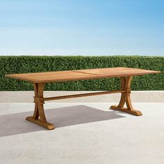 a wooden table sitting on top of a cement floor next to a green hedge covered wall