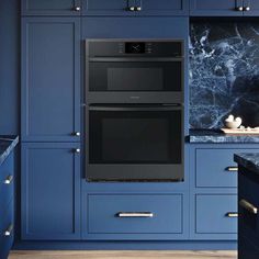 two black ovens in a blue kitchen with marble counter tops and cabinets on either side