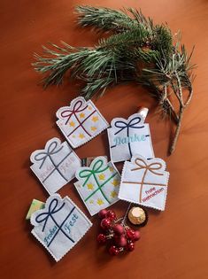 small cross stitch christmas ornaments on a wooden table next to a pine branch and bottle of wine