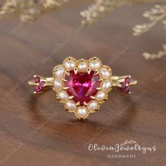 a ring with pearls and a heart shaped pink stone in the center on a wooden surface