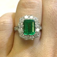 an emerald and diamond ring on someone's finger