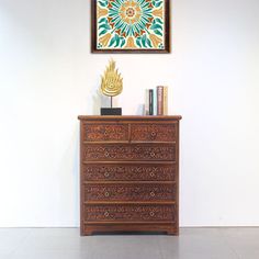 an ornate wooden dresser in front of a wall with a painting on the wall above it