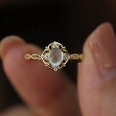 a close up of a person holding a gold ring with a white stone in it