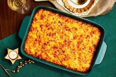 a green casserole dish with cheese on it next to two glasses of wine