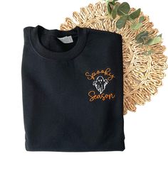 Our new Spooky Season Halloween Sweatshirt is the perfect addition to your Fall and Halloween wardrobe. This embroidered sweatshirt is professionally embroidered and will definitely get you excited for Fall and Halloween!  Professionally embroidered with left chest placement.  Sweatshirt is a 8 oz. 50/50 cotton/polyester blend fleece Spooky season will be embroidered with our premium orange thread. The ghost will be embroidered with black thread on the following colors - White, Sand, Light Blue, Black Embroidered T-shirt For Fall, Black Cotton Halloween Sweater, Black T-shirt With Custom Embroidery For Fall, Black Embroidered Tops For Halloween, Halloween Embroidered Cotton Sweatshirt, Custom Embroidered Long Sleeve Top For Halloween, Embroidered Cotton Sweatshirt For Halloween, Black T-shirt With Embroidered Logo For Fall, Black Embroidered Logo T-shirt For Fall