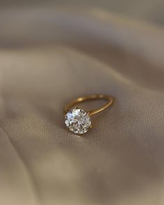 a diamond ring sitting on top of a satin material covered surface with a gold band