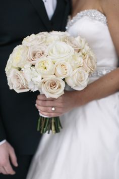 a bride and groom holding a bouquet of white roses